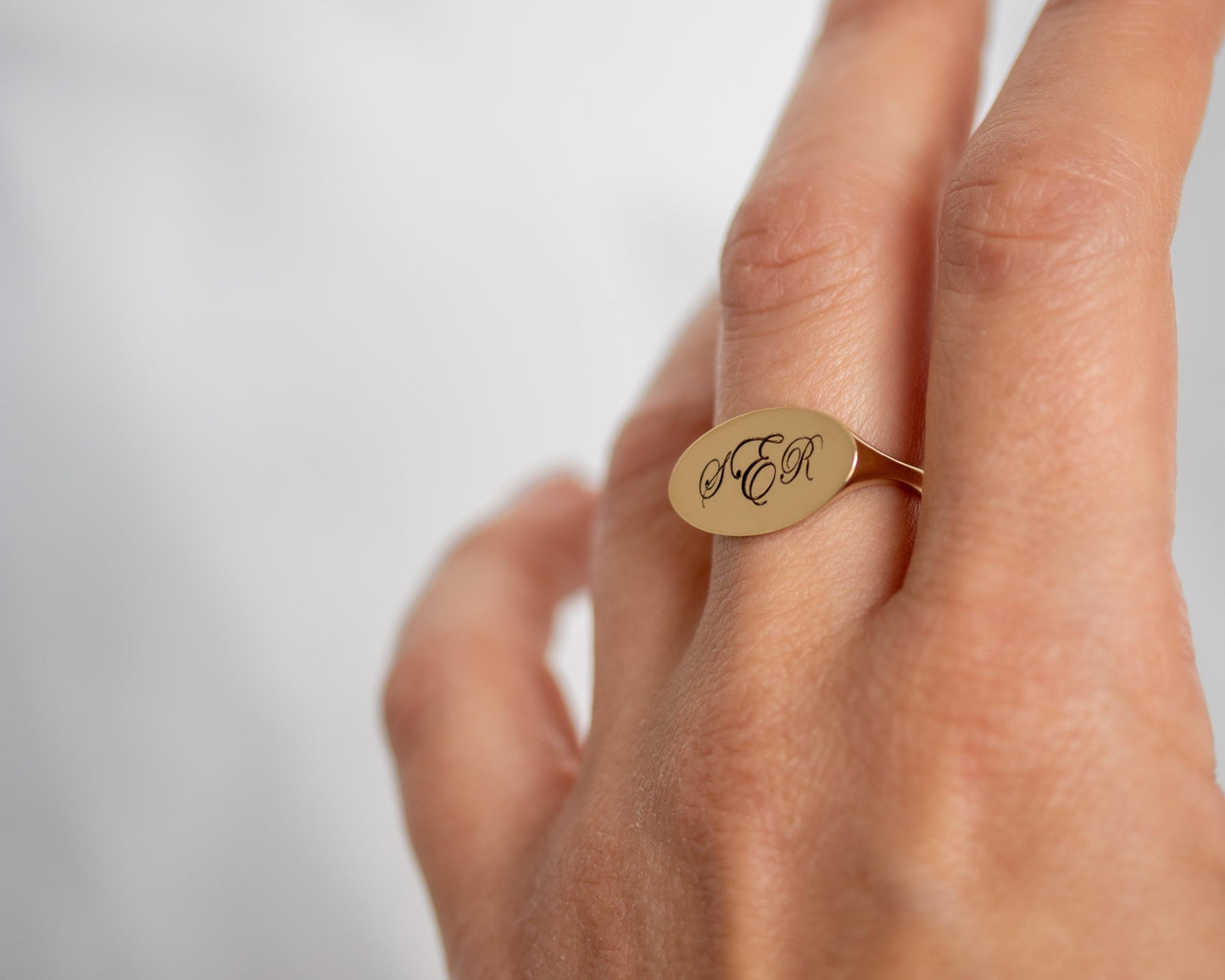 Gold ring with engraved initials on a hand against a light background