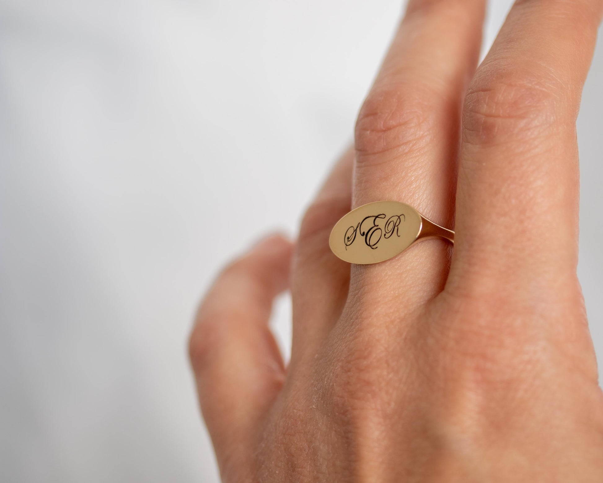 Gold ring with engraved initials on a hand against a light background