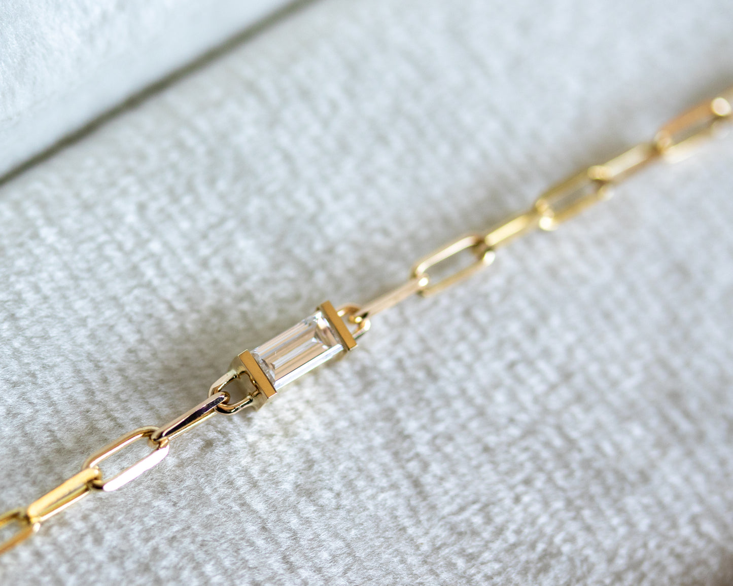 Gold chain bracelet with baguette cut diamond on a textured white surface