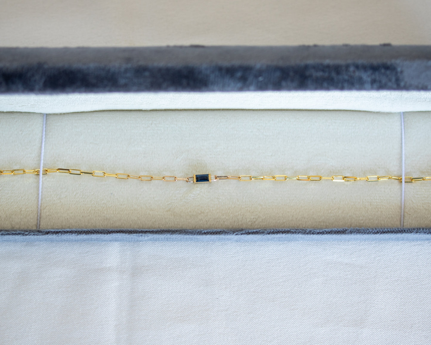 Gold bracelet with a blue baguette cut sapphire in white gray jewelry case 