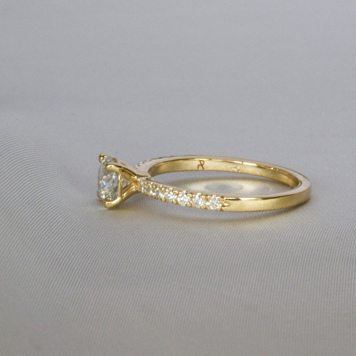 Angled view of a pavé diamond solitaire engagement ring in yellow gold