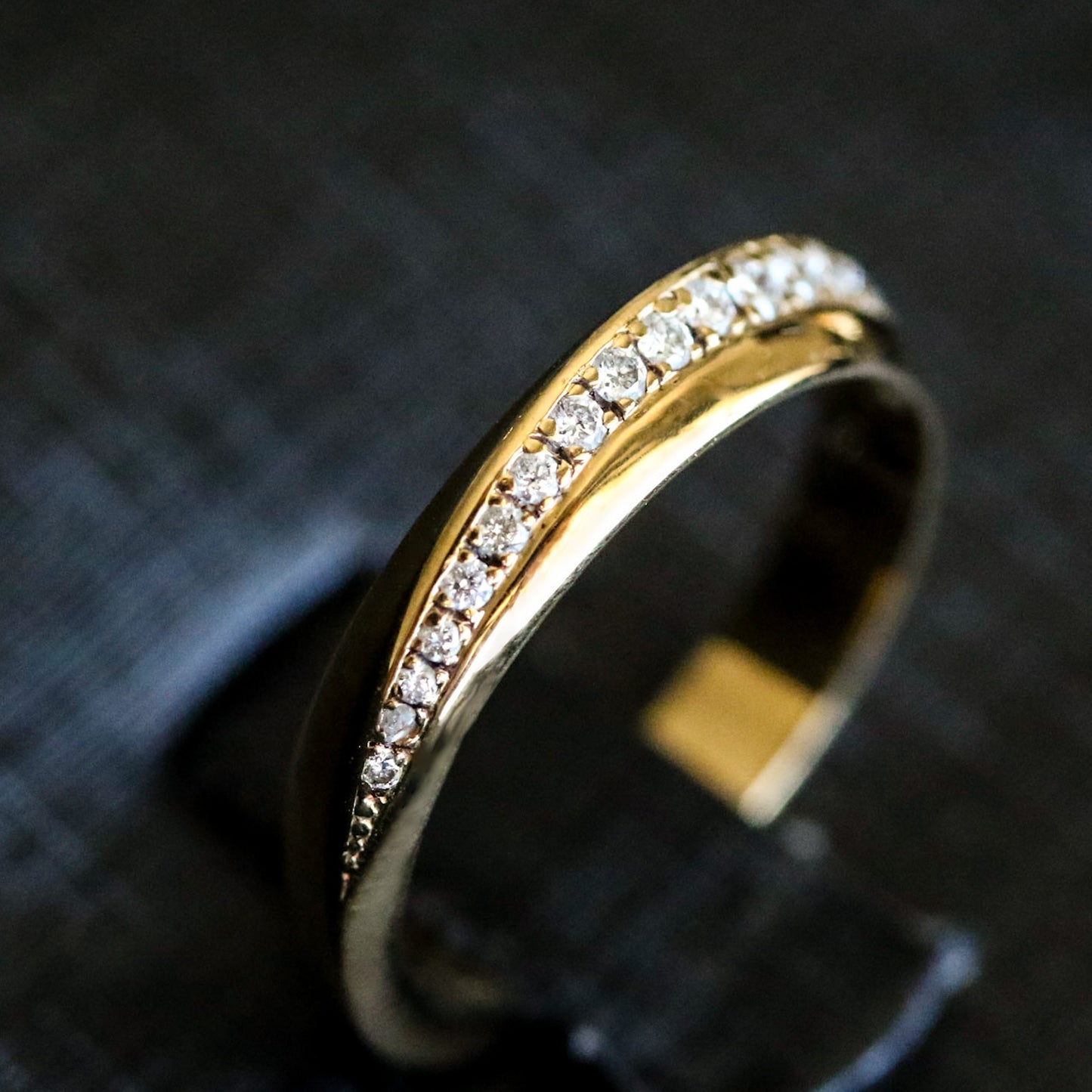 A gold band ring with a twisted geometric design and a pave of round-cut natural diamonds set within it.