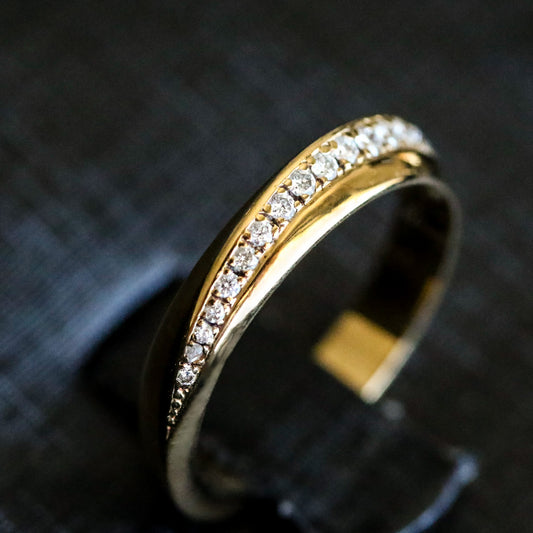 A gold band ring with a twisted geometric design and a pave of round-cut natural diamonds set within it.