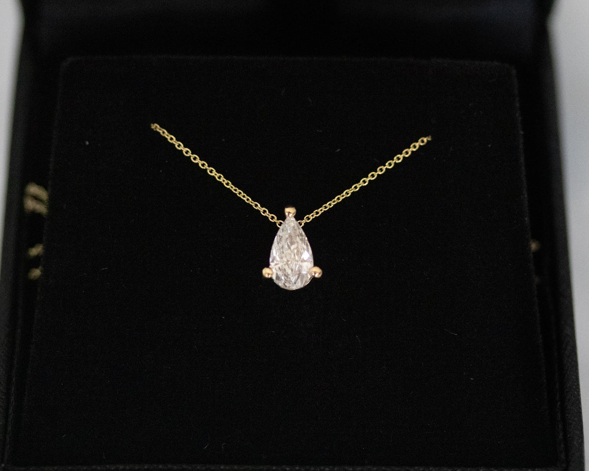 Pear diamond solitaire pendant on a 14K yellow gold chain against a black background