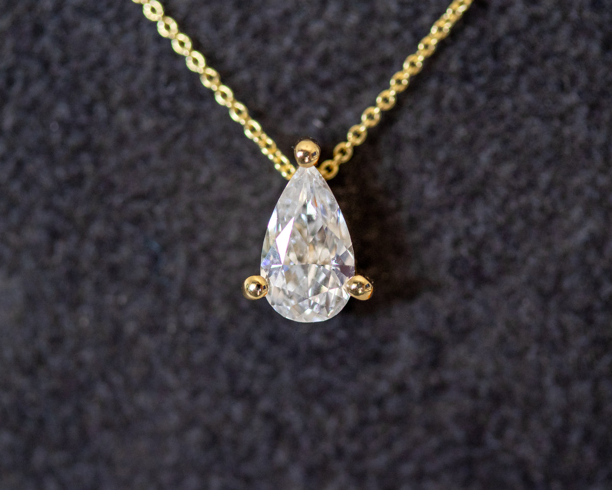 Close-up of a pear diamond solitaire pendant in a three-prong setting on a 14K yellow gold rolo chain