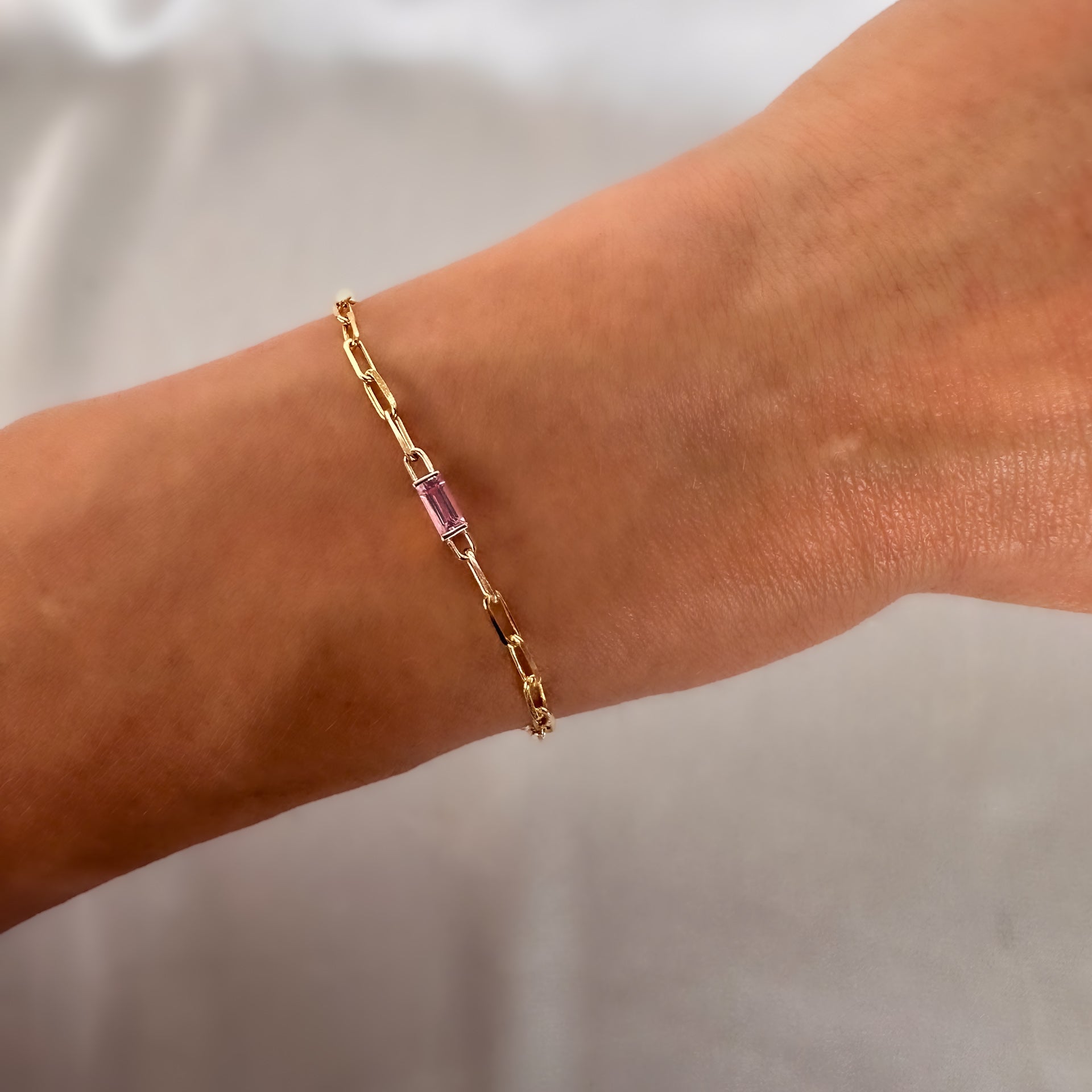 yellow gold paperclip chain bracelet with baguette cut pink sapphire on a women's hand