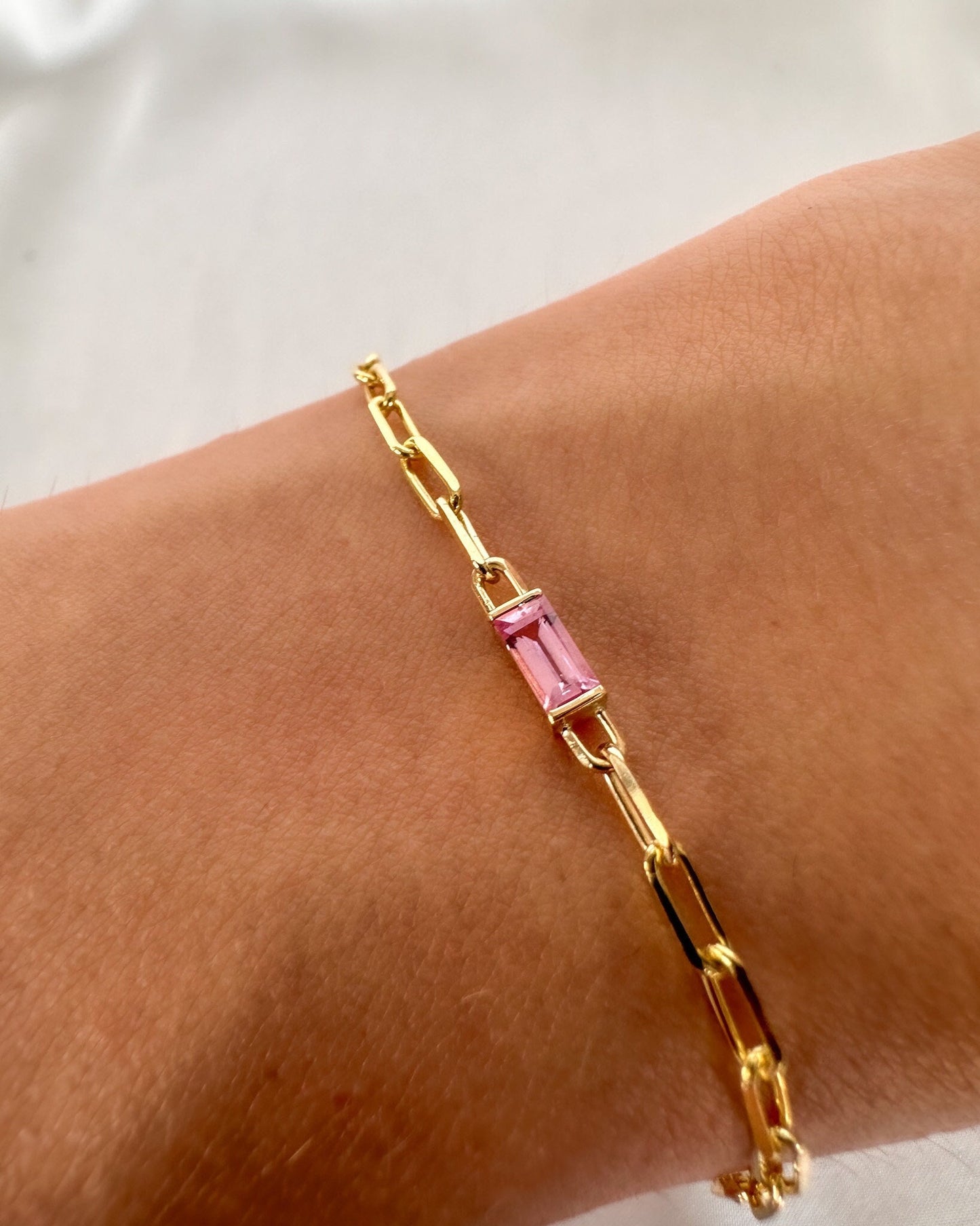 Gold bracelet with a pink gemstone on a wrist against a white background