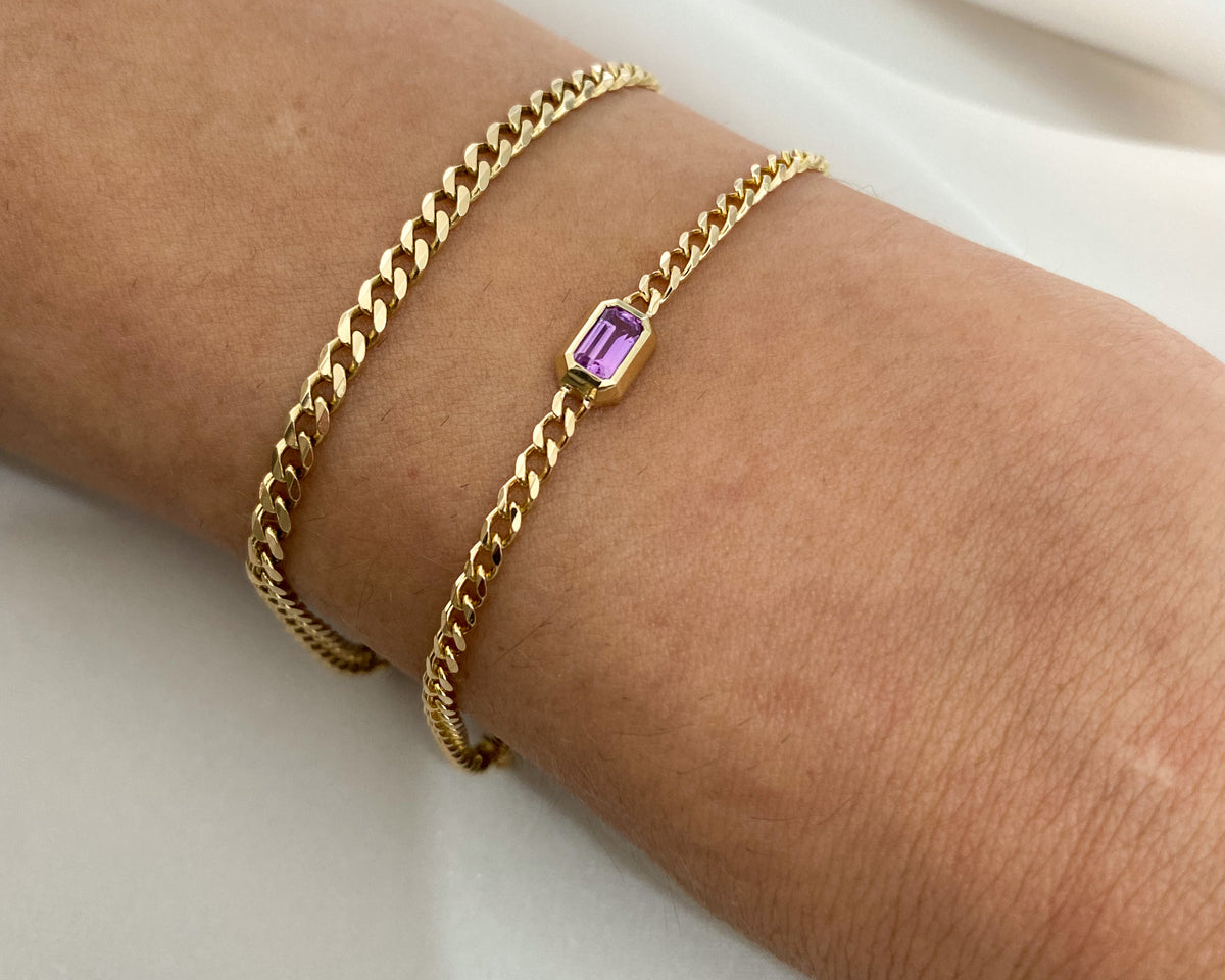 14K yellow gold fine curb chain bracelet with a bezel-set emerald cut pink sapphire, worn on the wrist with a plain curb chain bracelet