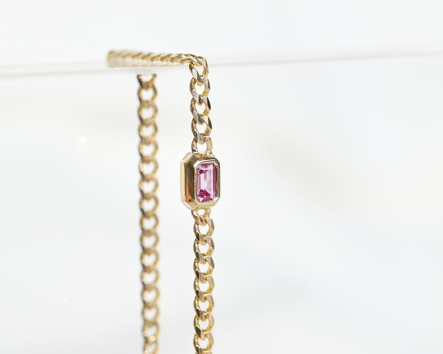 Close-up of a 14K yellow gold curb chain bracelet with emerald cut pink sapphire
