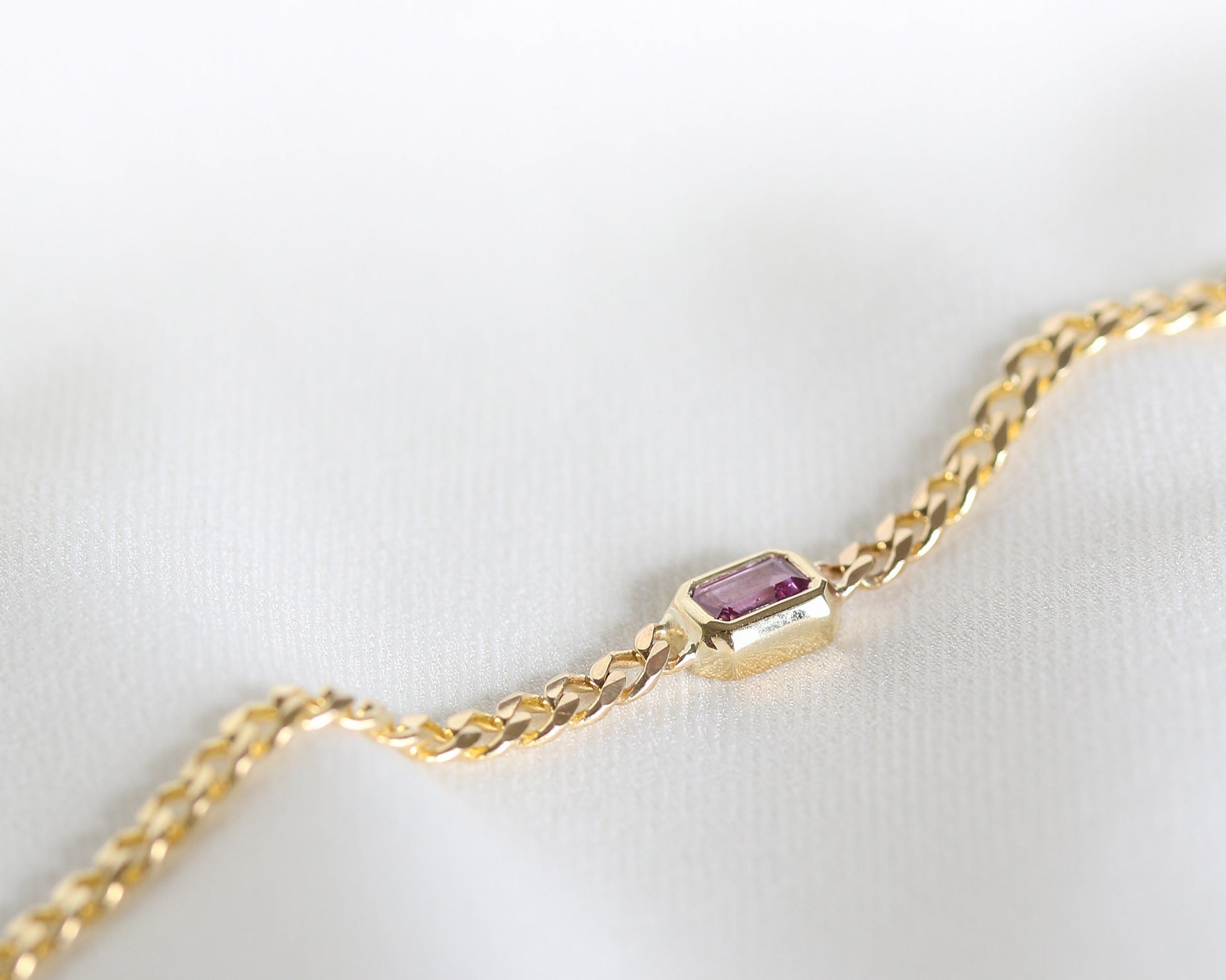 14K yellow gold curb chain bracelet with emerald cut pink sapphire, angled close-up