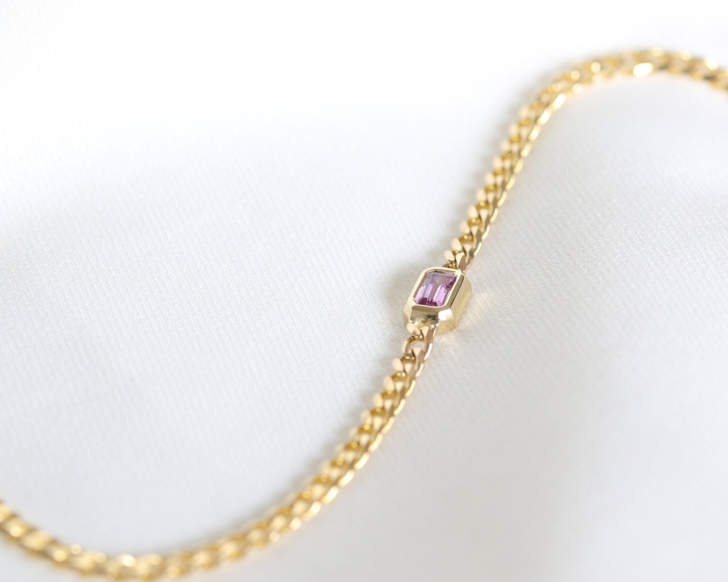 14K yellow gold curb chain bracelet with emerald cut pink sapphire, soft focus close-up