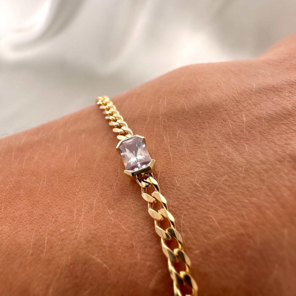 Fine 14K yellow gold curb chain bracelet with an emerald cut pink sapphire, worn on the wrist