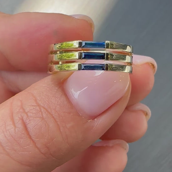 A minimalist gold ring with three blue baguette cut sapphires set close together, creating a light and unique appearance displayed in womens hand