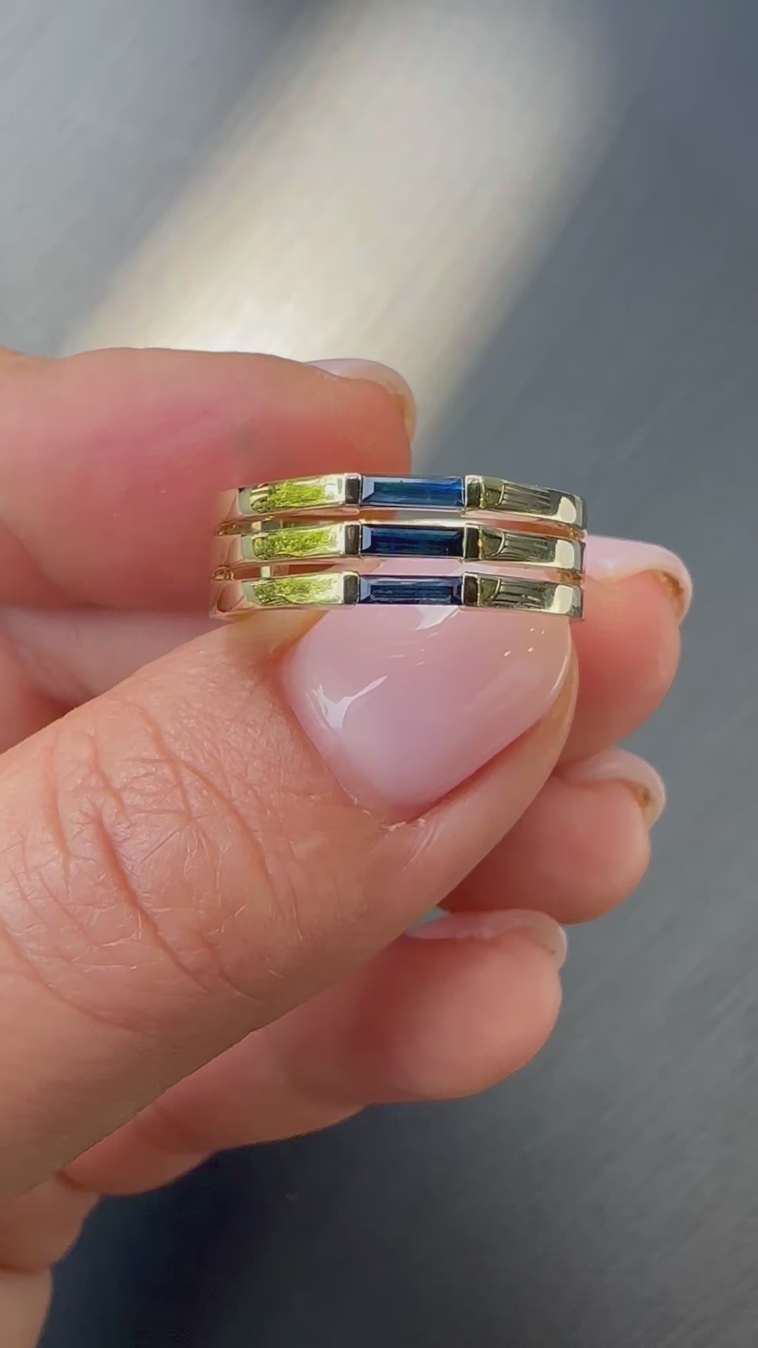 A minimalist gold ring with three blue baguette cut sapphires set close together, creating a light and unique appearance displayed in womens hand