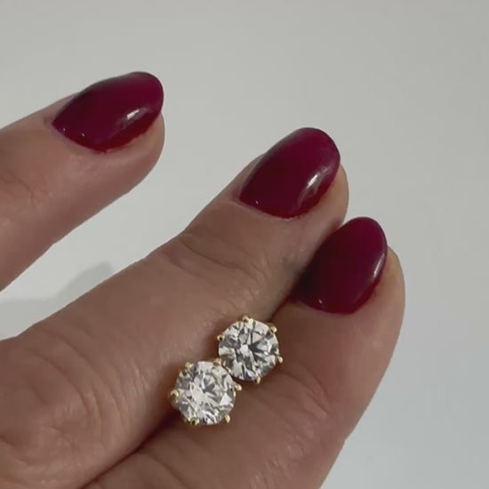Round diamond stud earrings in 14K gold, shown held in the hand