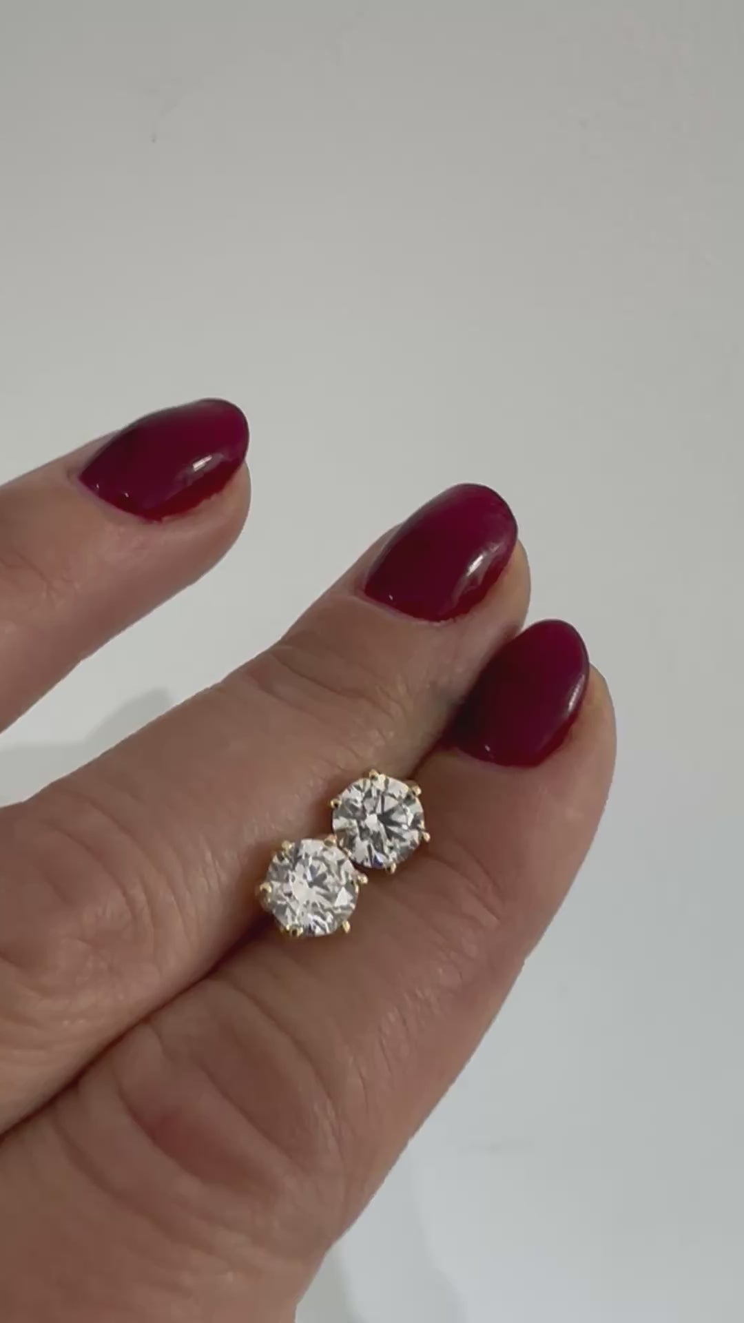 Round diamond stud earrings in 14K gold, shown held in the hand