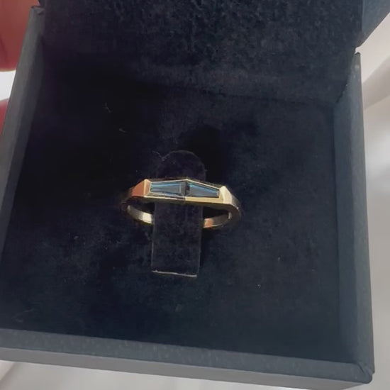 A minimalist gold ring with two blue baguette cut sapphires set in a box, with the ring displaying a tapered design.