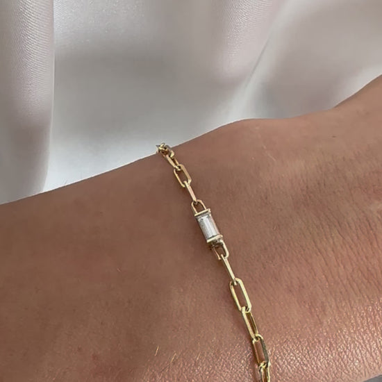 yellow gold paper clip chain bracelet with baguette cut diamond on person's wrist