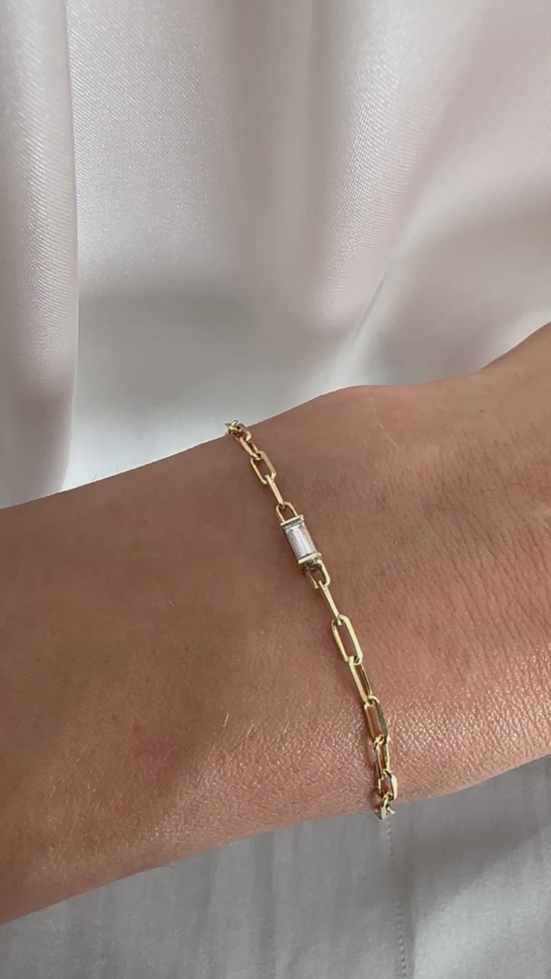 yellow gold paper clip chain bracelet with baguette cut diamond on person's wrist