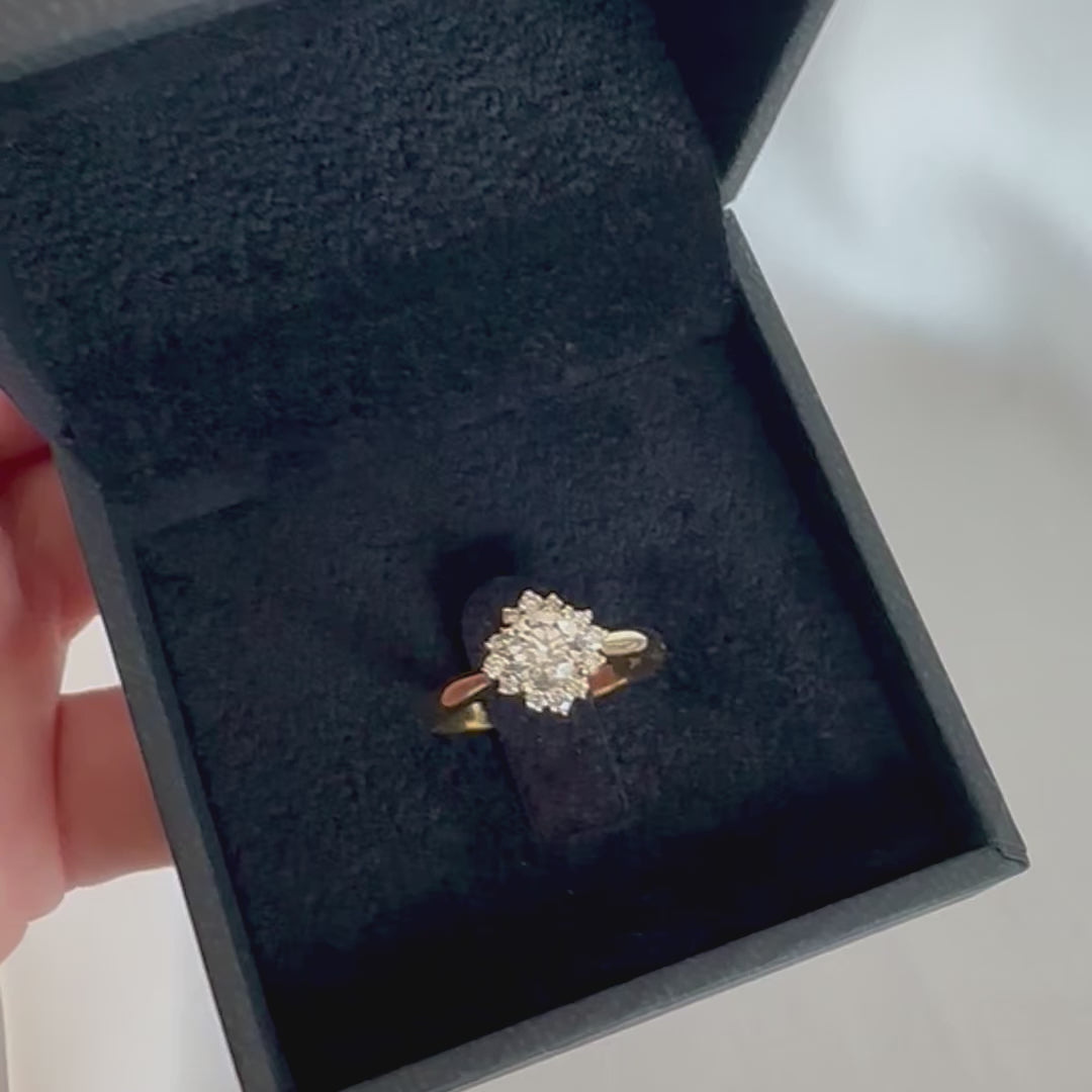 A floral engagement ring with a central diamond and smaller surrounding diamonds set in a 14K gold band displayed in black velvet box
