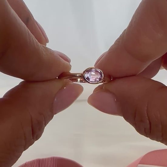 14K gold bezel-set oval pink sapphire ring — shown and worn on finger