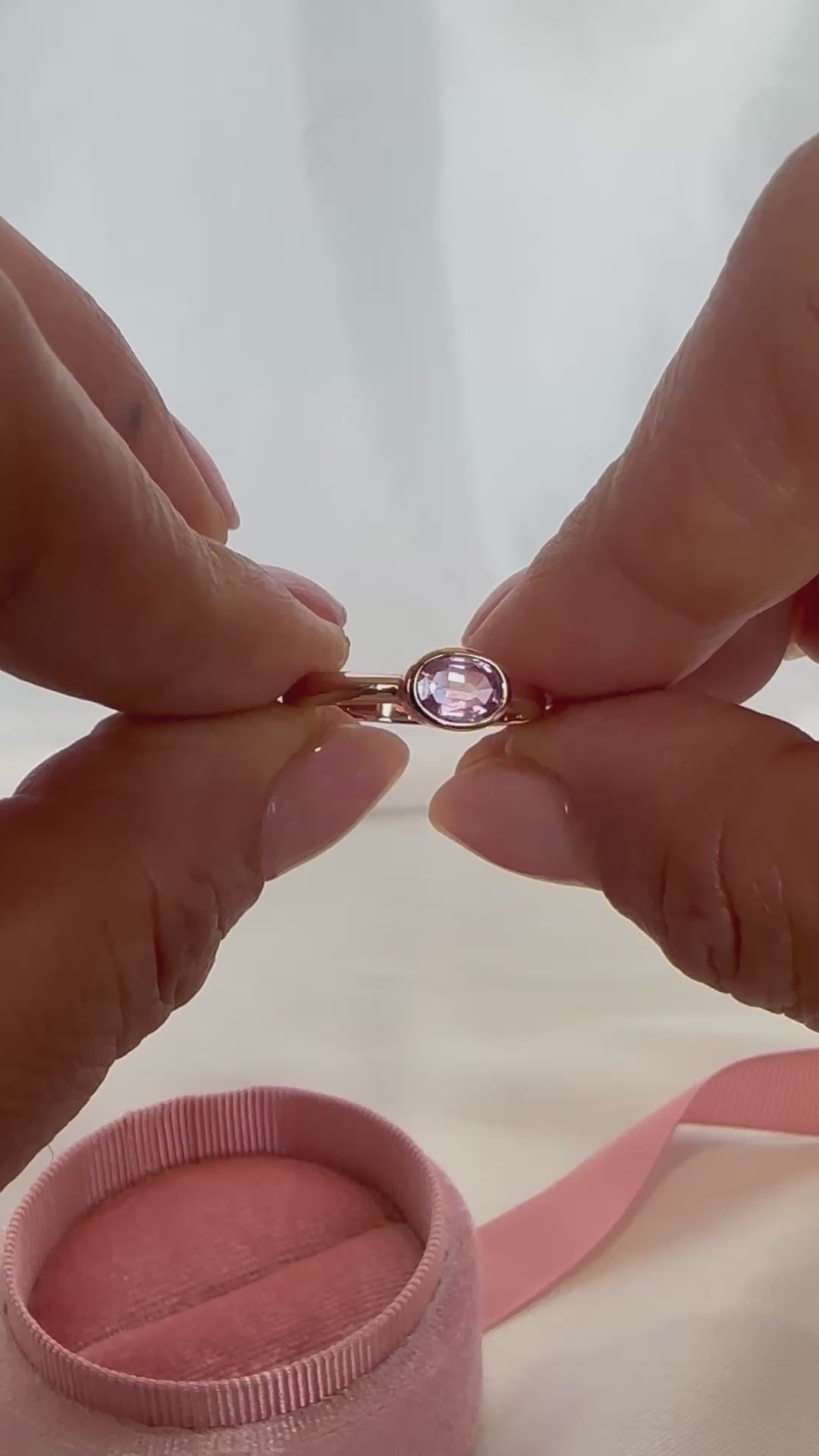 14K gold bezel-set oval pink sapphire ring — shown and worn on finger