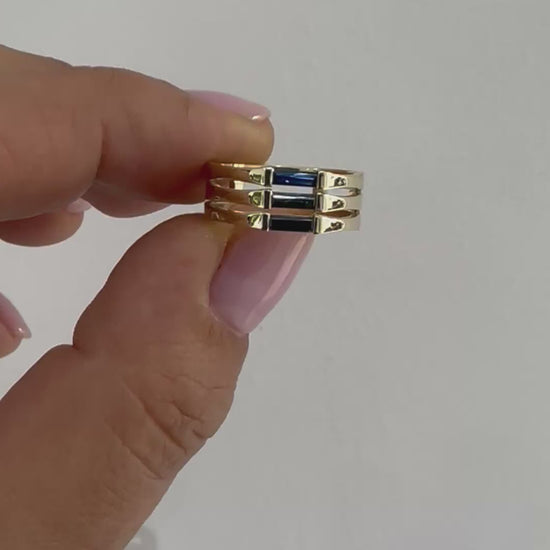 A minimalist gold ring with three blue baguette cut sapphires set close together, creating a light and unique appearance displayed in womens hand