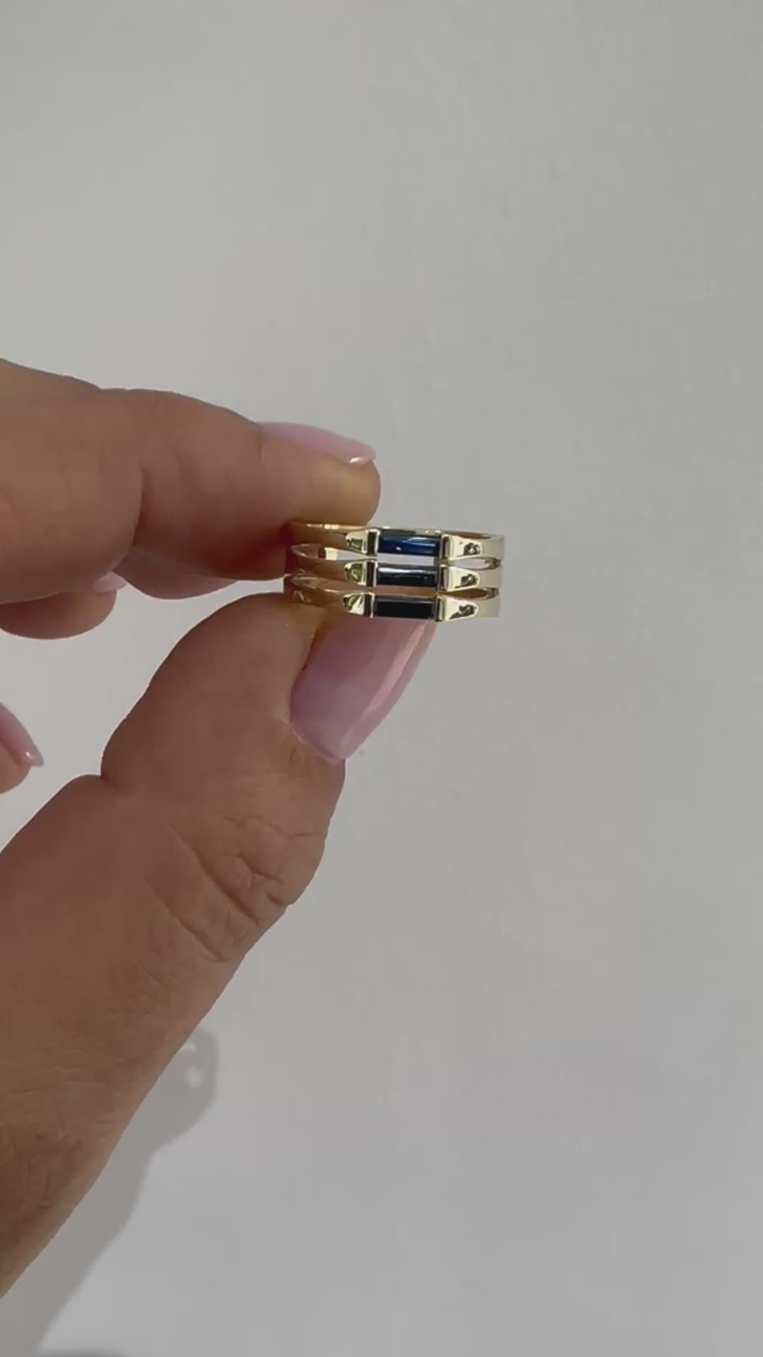 A minimalist gold ring with three blue baguette cut sapphires set close together, creating a light and unique appearance displayed in womens hand