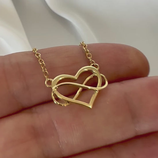 yellow gold heart and infinity symbol pendant and chain displayed in hand 