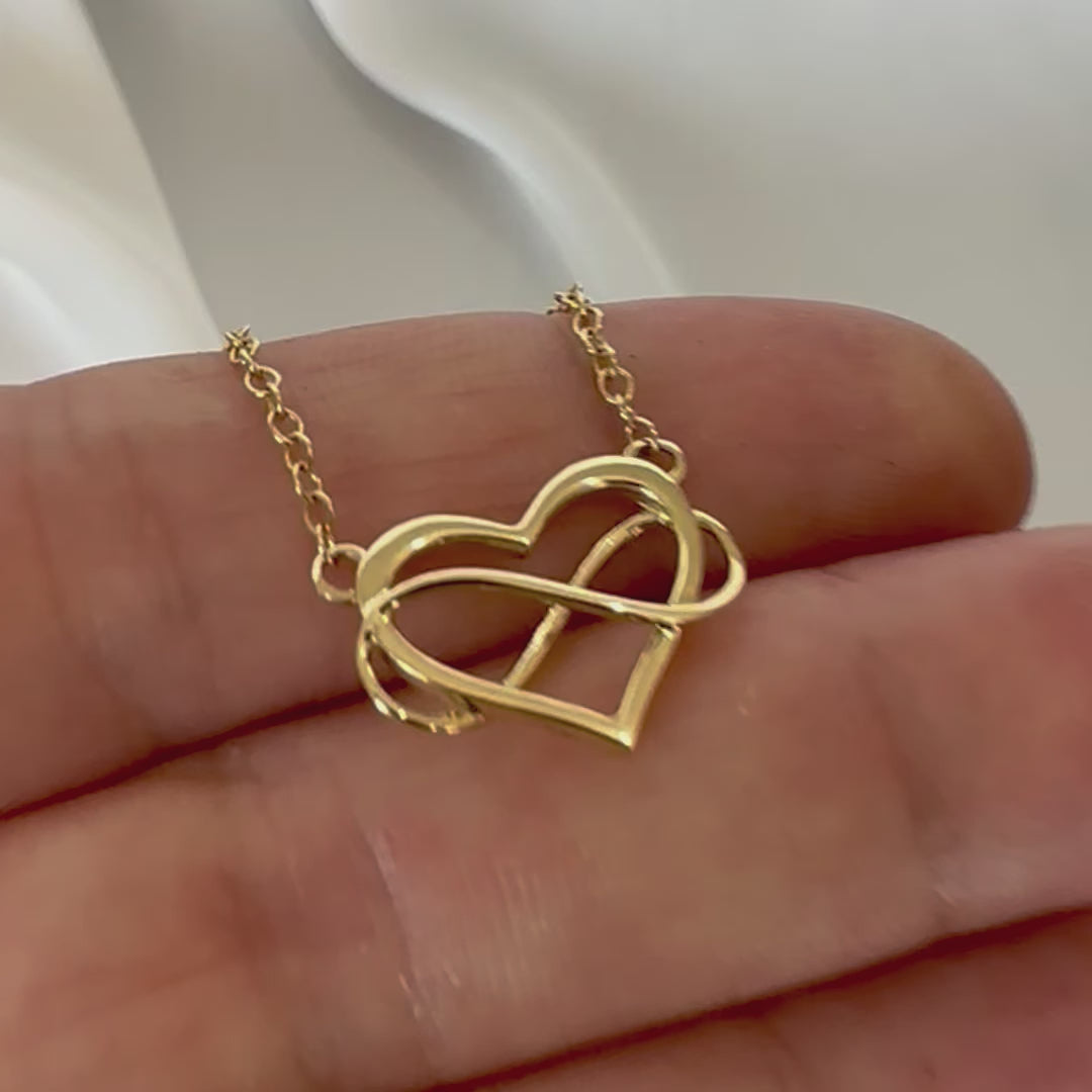 yellow gold heart and infinity symbol pendant and chain displayed in hand 