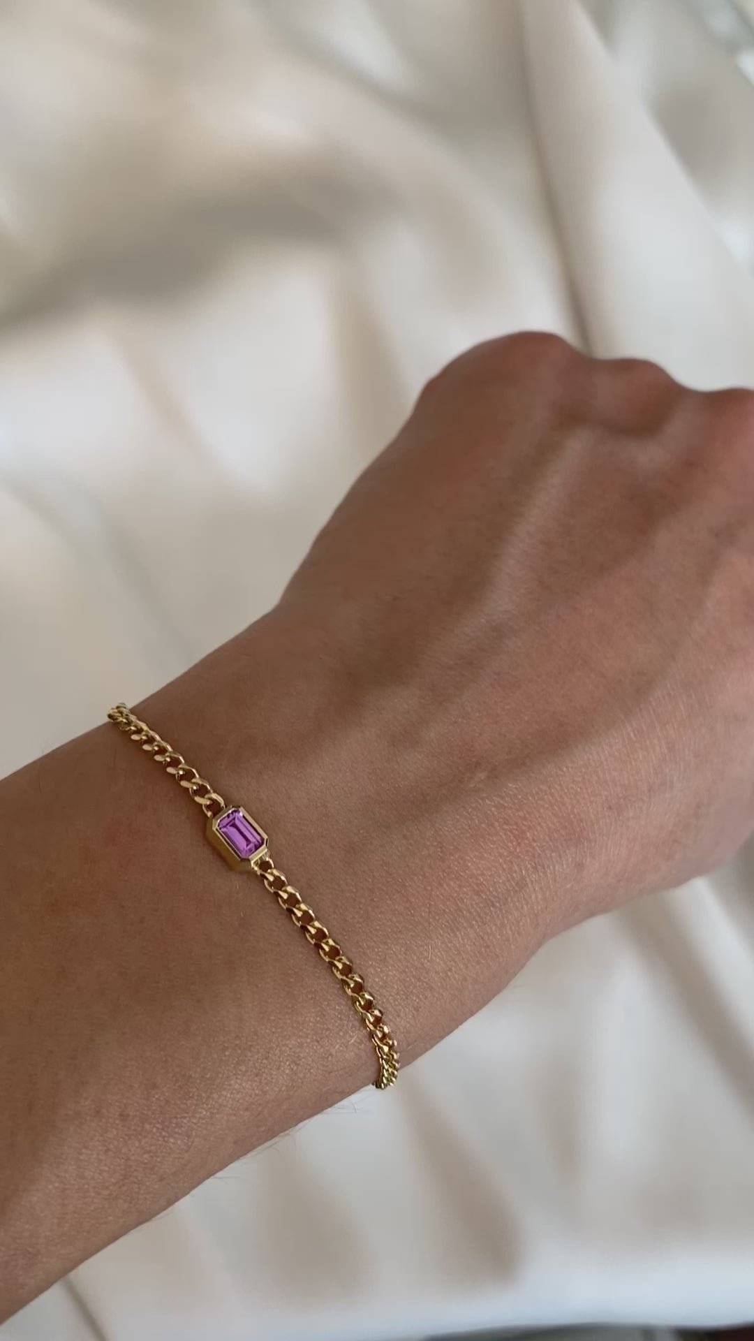 Short video of a 14K yellow gold curb chain bracelet with emerald cut pink sapphire worn on the wrist