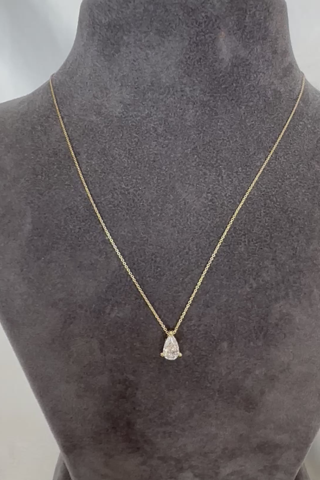 Pear diamond solitaire necklace in 14K gold displayed on a gray velvet torso stand