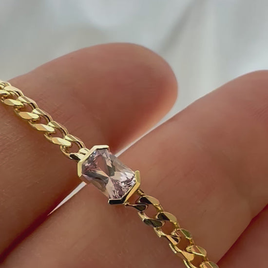 A gold bracelets with a curb chain design one featuring an emerald cut natural pink sapphire displayed in person's hand