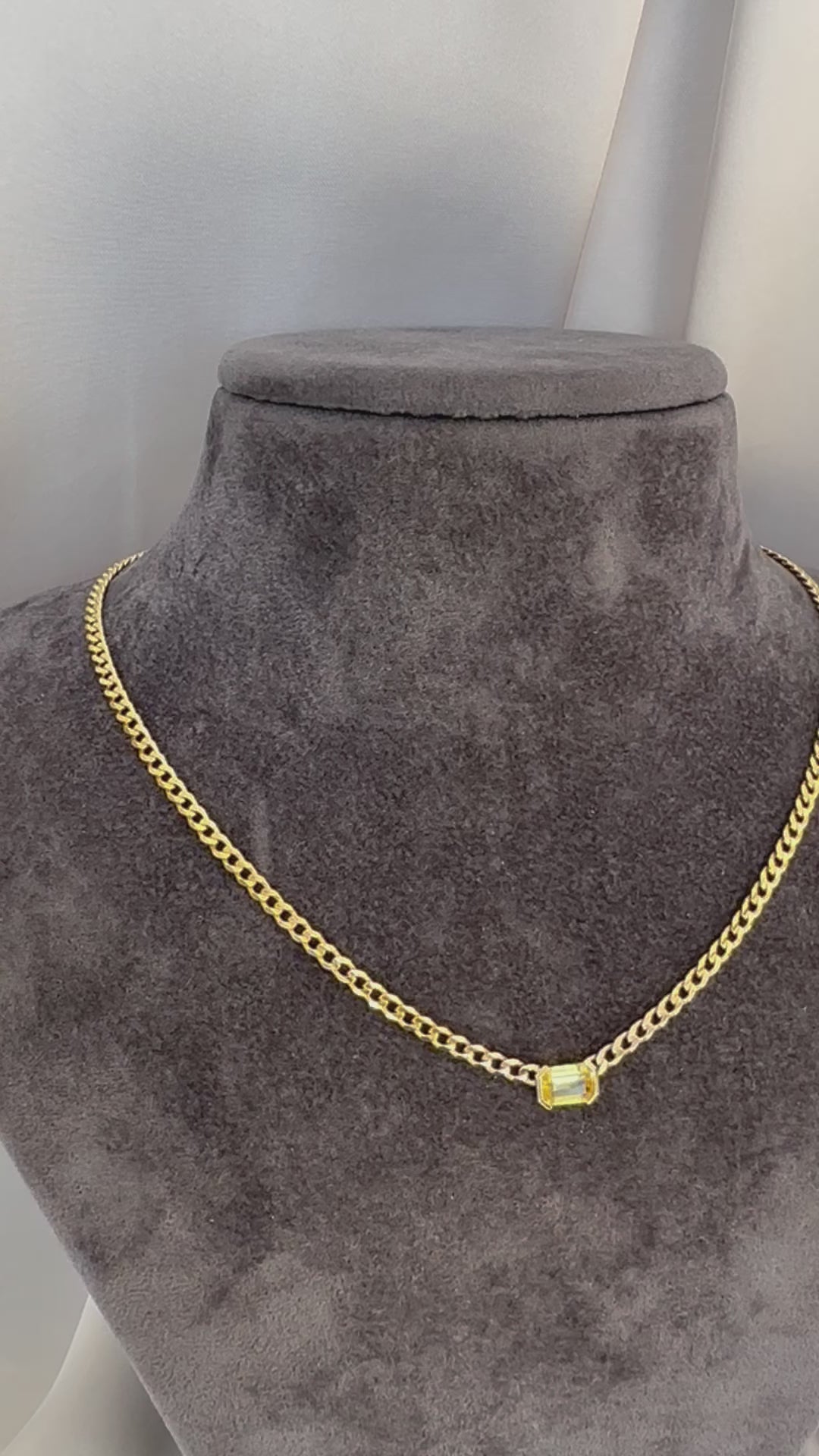A 14K gold yellow sapphire solitaire necklace with an emerald cut natural sapphire pendant on gray texture torso