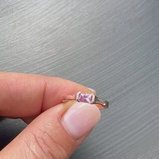 A rose gold ring with a emerald cut natural pink sapphire stone, set in a half bezel setting displayed in womens hand