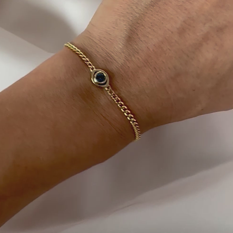 gold curb chain bracelet with a blue sapphire set in a evil eye centerpiece shown on person's wrist.