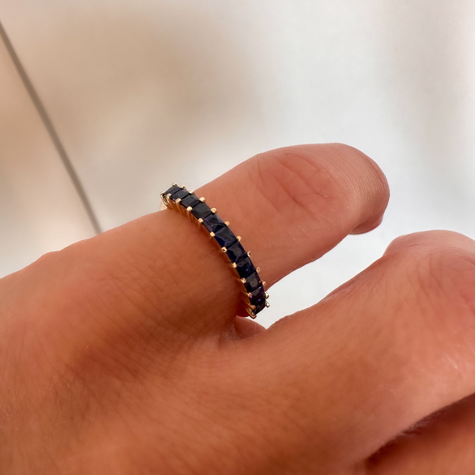 close up of a princess cut blue sapphire eternity ring displayed on women's pinky finger