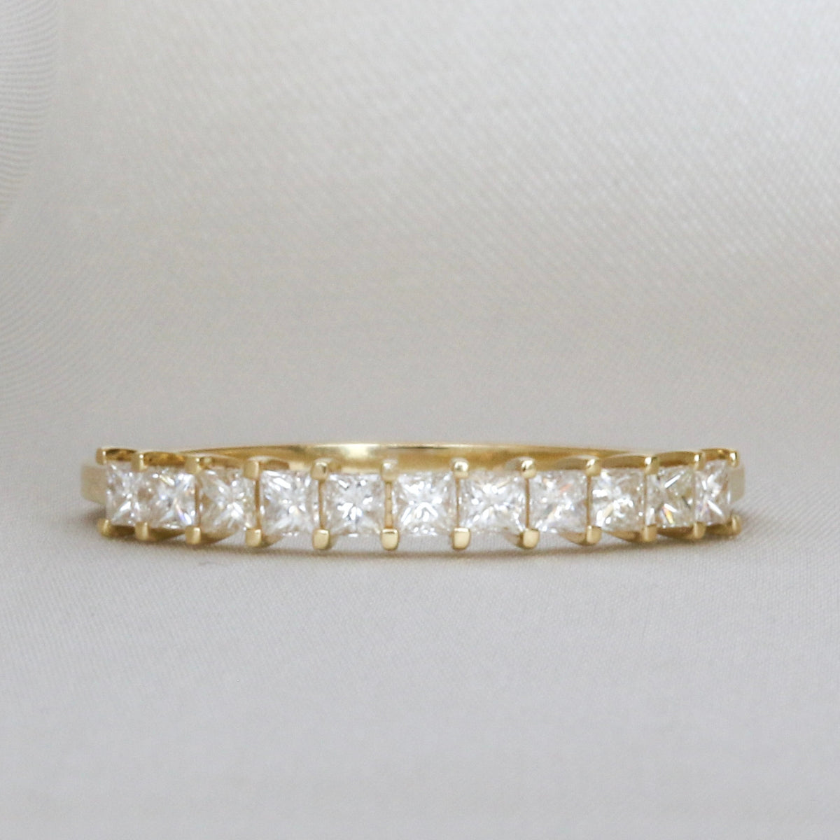 Princess cut diamond half eternity band in 14K yellow gold, front view on light gray fabric