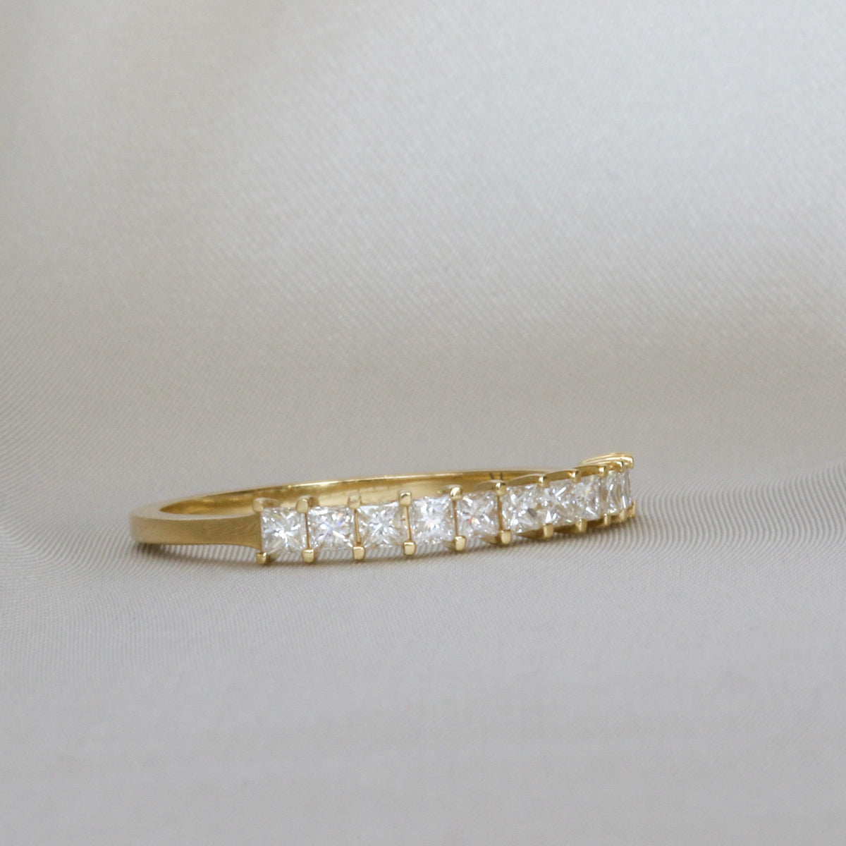 Princess cut diamond half eternity band in 14K yellow gold, angled side view on light gray fabric