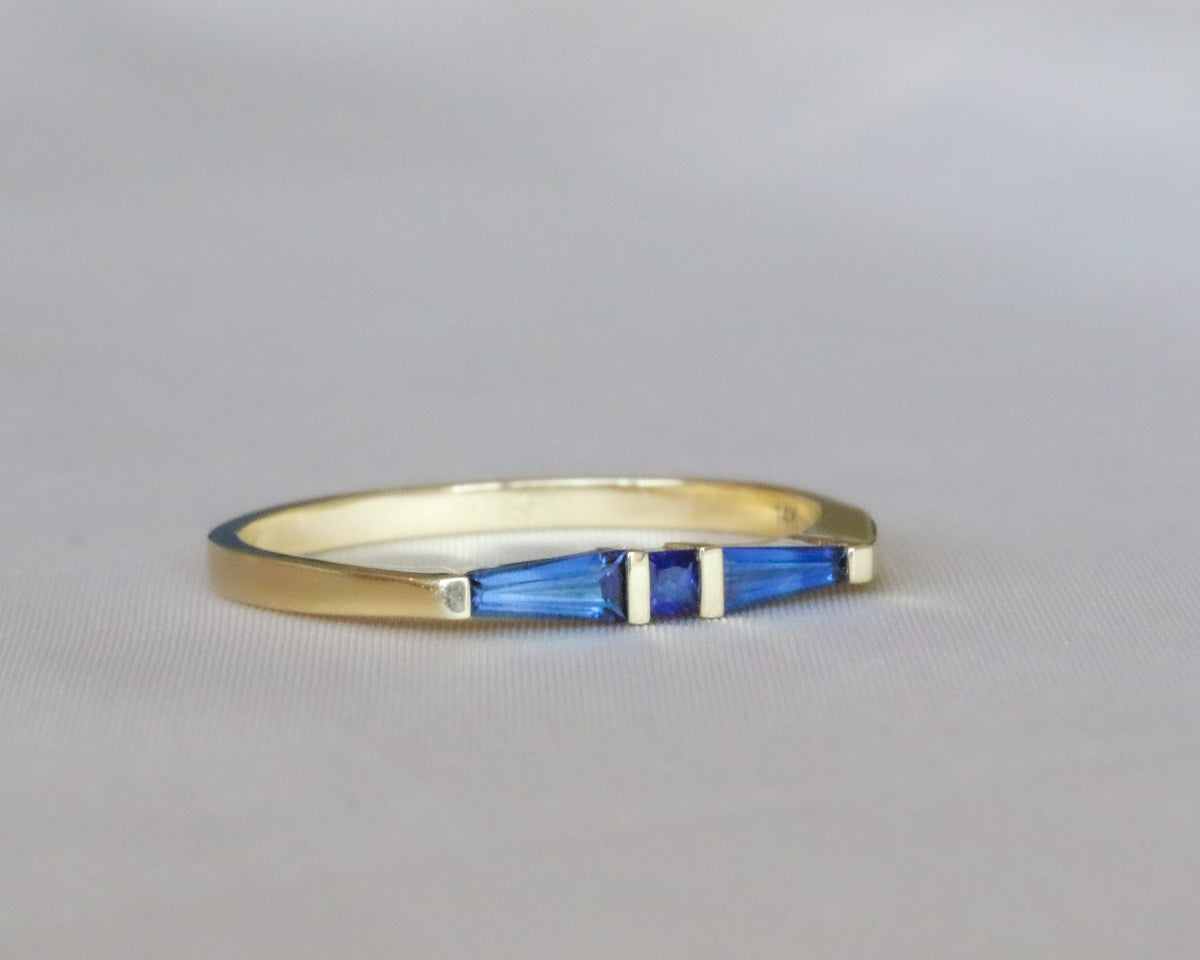 Front view of a princess-cut and tapered baguette blue sapphire ring in yellow gold on a gray background