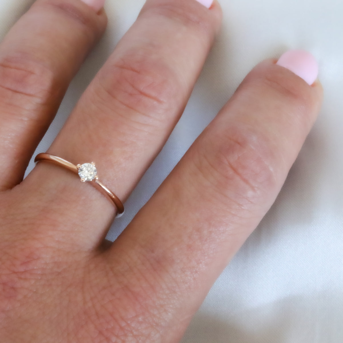 Rose gold four-prong diamond solitaire ring on the finger, close-up