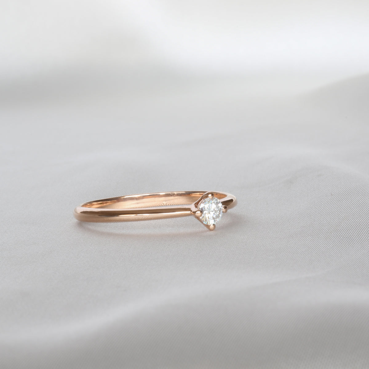 Dainty rose gold four-prong diamond solitaire ring on a white background