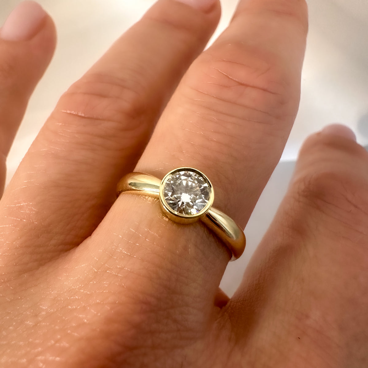 Close-up of a round brilliant diamond in a smooth gold bezel, worn on the hand
