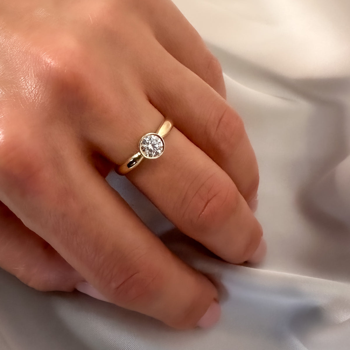 Bezel set round diamond ring in yellow gold on the hand