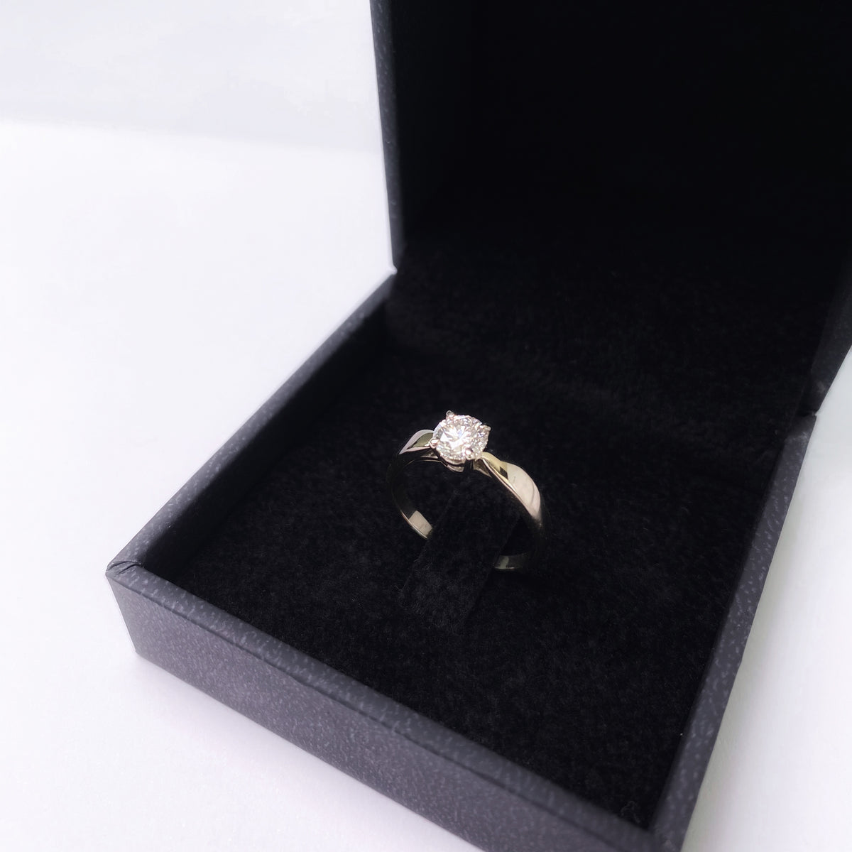 Round diamond solitaire ring with cathedral shoulders in a black jewelry box, angled view