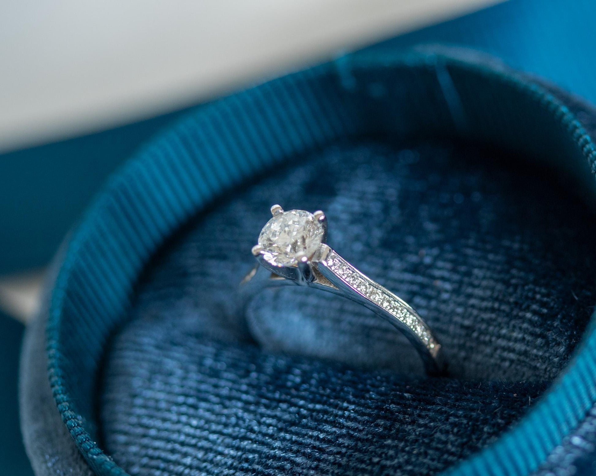 Round brilliant diamond engagement ring in 14K white gold with pavé band, modern solitaire design in blue velvet box