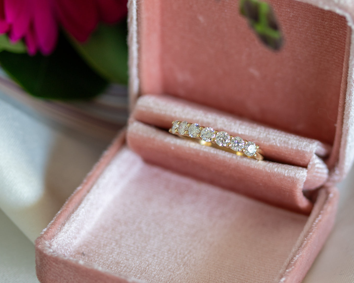 Gold round diamond eternity ring displayed in an open jewelry box with flowers