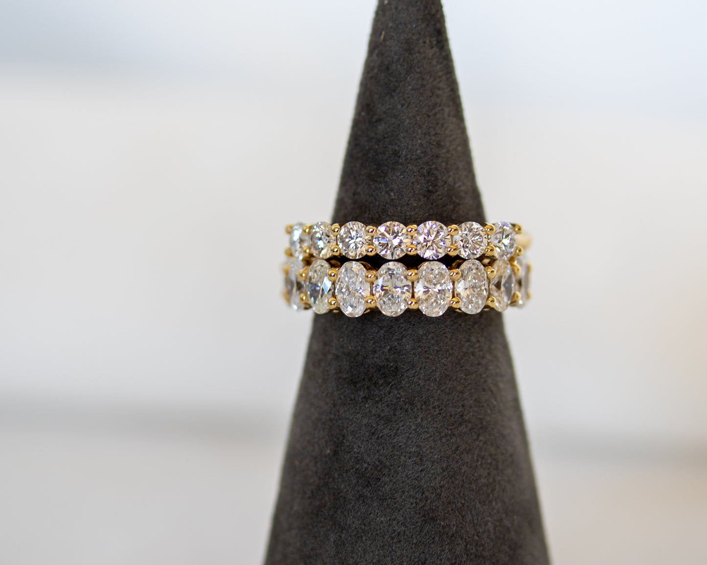 Gold round diamond eternity ring displayed on a ring display cone