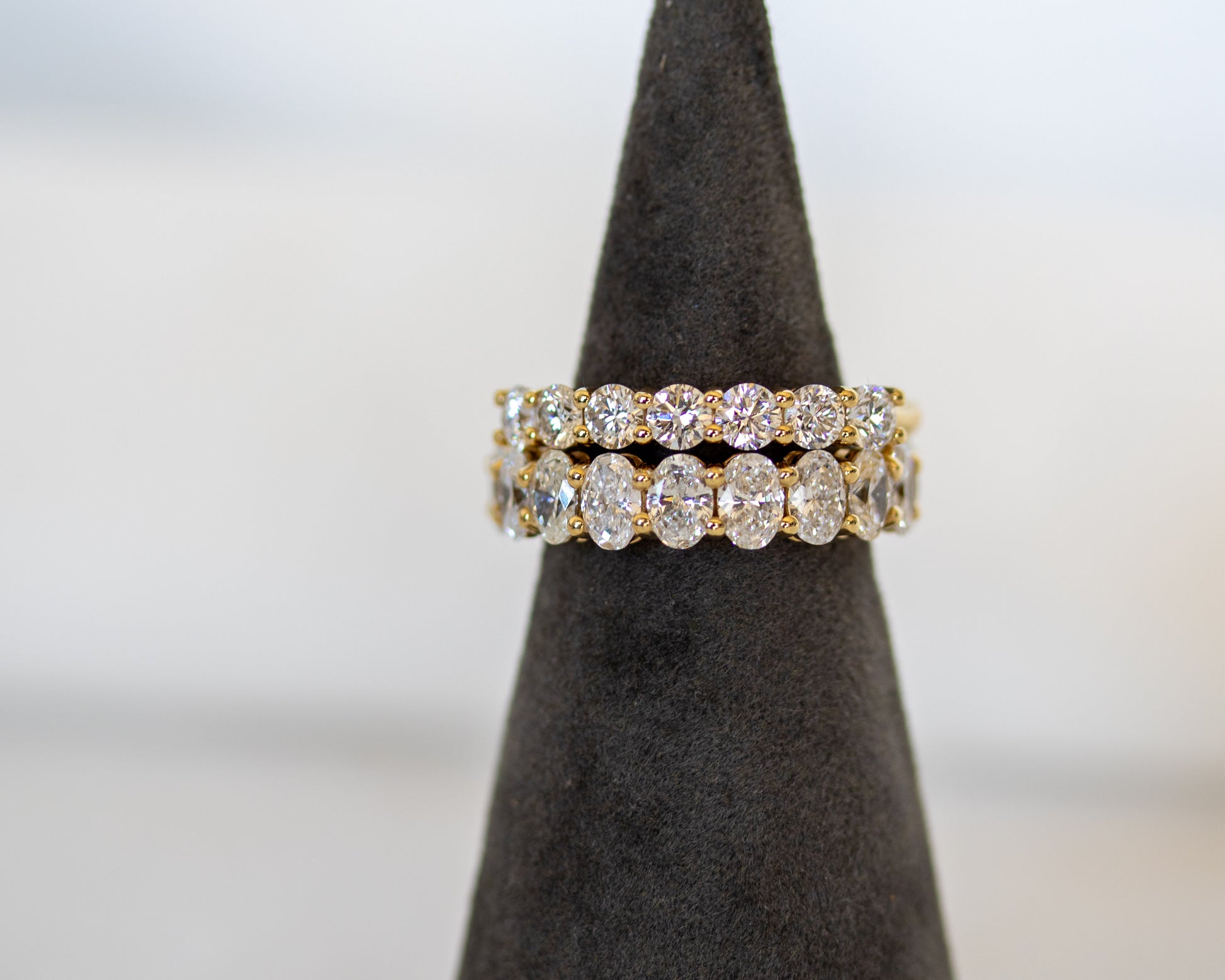 Gold round diamond eternity ring displayed on a ring display cone
