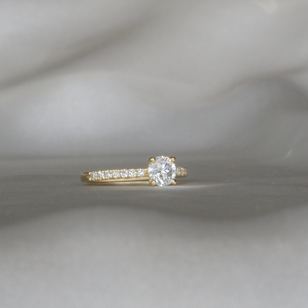 Profile of a round diamond solitaire ring with a pavé band in yellow gold on a gray background